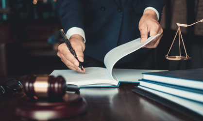 Lawyer writing in a book sitting on a desk with a gavel, books, and scales