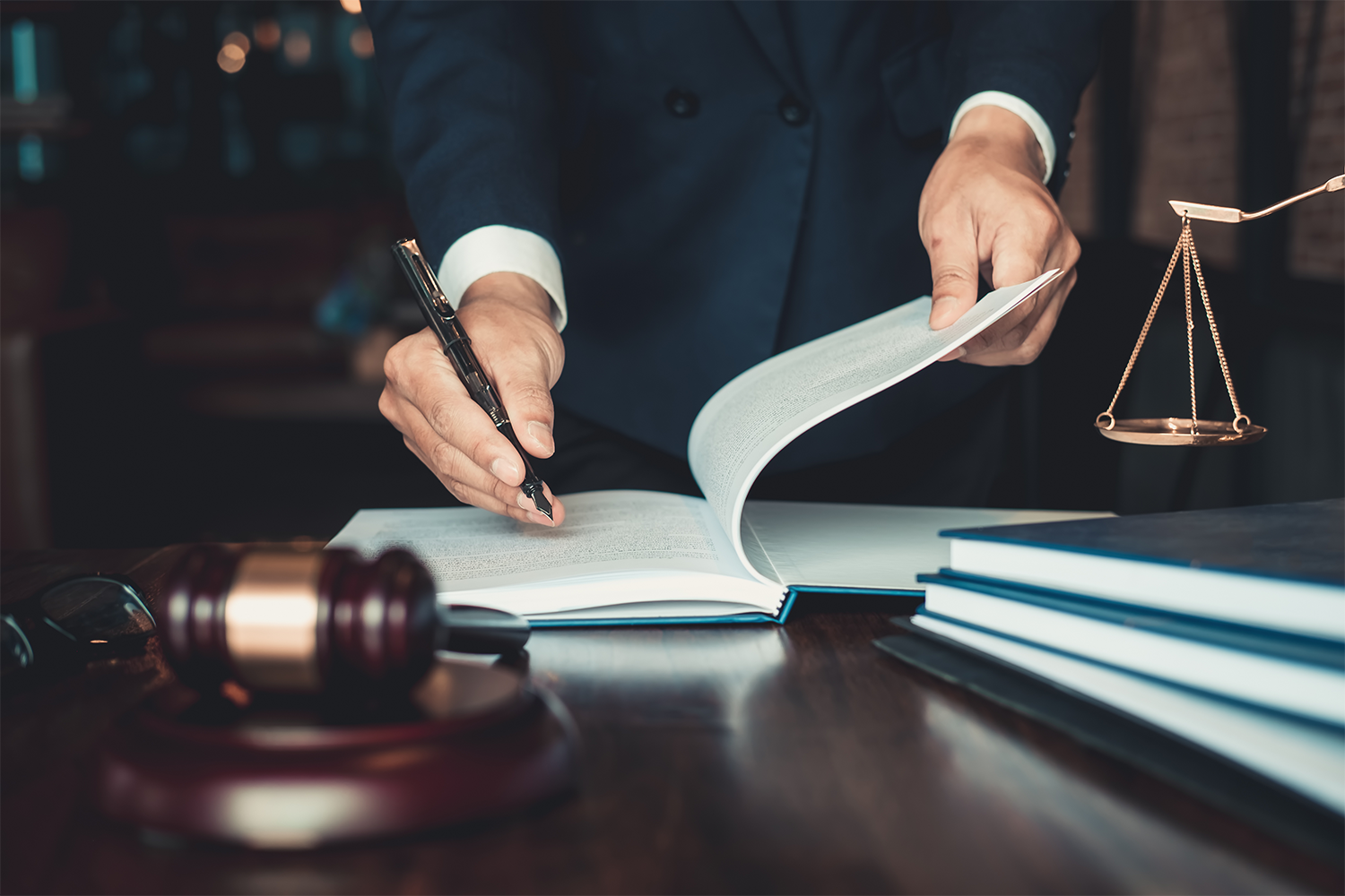 Lawyer writing in a book sitting on a desk with a gavel, books, and scales