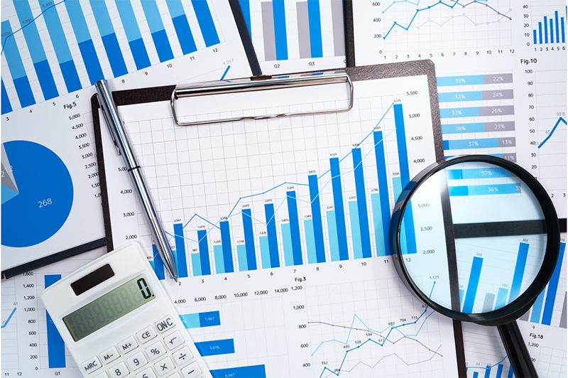 Various blue charts, some of which are on a clipboard with a pen, calculator, and magnifying glass on top of it.