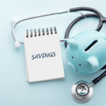 A small spiral notebook with the word savings written on it next to a light blue piggy bank with a stethoscope around it on a light blue background