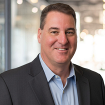 Caucasian man with short brown hair wearing a light blue button up shirt and a charcoal gray jacket.